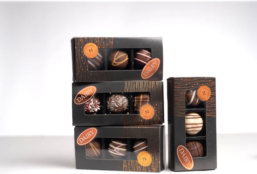 An elegant dark colored box containting 3 truffles, each with a fancy ribbon decorating the outside.