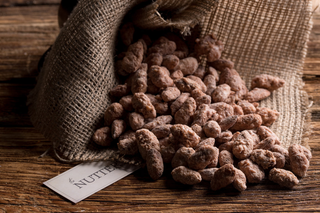 Sweet roasted almonds coated in a cinnamon-sugar glaze, displayed in a rustic burlap-style bag.