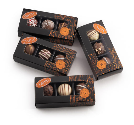 A sophisticated black box containing three handcrafted truffles with assorted toppings, ideal for chocolate lovers and gift-giving.