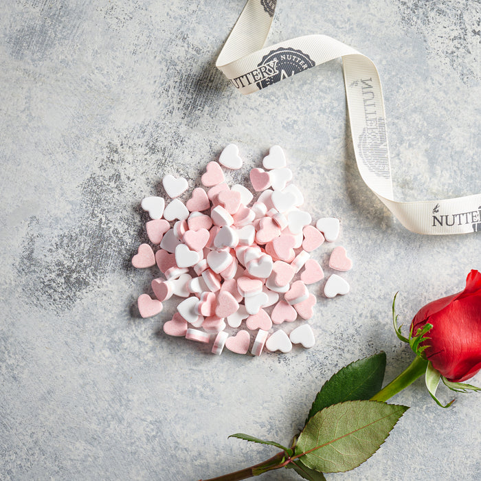 A romantic arrangement of pink and white heart-shaped candies, accompanied by a red rose and The Nuttery ribbon.