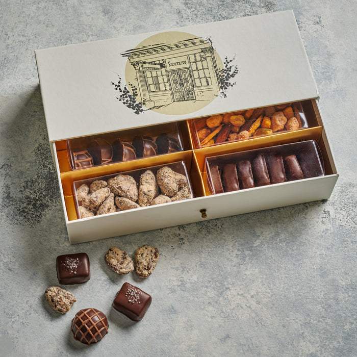A sophisticated gift box featuring an illustration of The Nuttery storefront, filled with an assortment of gourmet chocolates, nuts, and specialty confections.