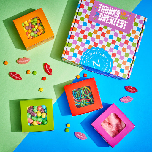 Colorful candy gift boxes with sour and chewy treats, surrounded by gummy lips and candy pieces, displayed on a green and blue background with the message "Feel the magic in every bite" inside the box lid