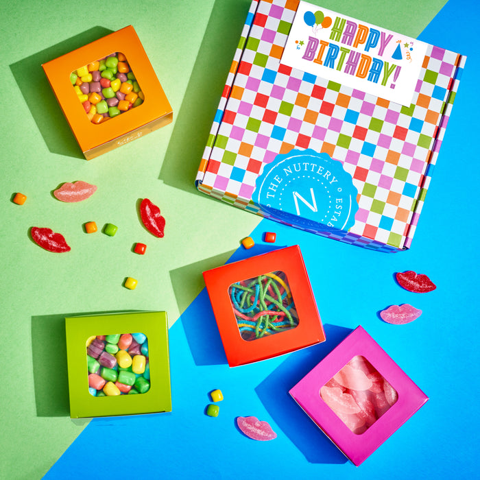 Colorful assortment of candy boxes featuring sour and chewy treats, surrounded by gummy lips and candy pieces, displayed on a vibrant green and blue background with a festive "Happy Birthday" gift box in the center