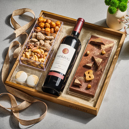 A sophisticated wine and gourmet gift set featuring a bottle of fine red wine, gourmet chocolate, and premium nuts, elegantly arranged in a wooden tray.