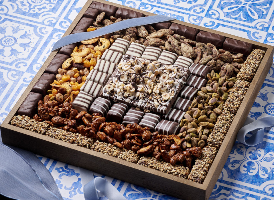 Close-up view of the gourmet snack tray highlighting the intricate arrangement of chocolates, nuts, pistachios, and dried fruits on a stylish blue table setting.