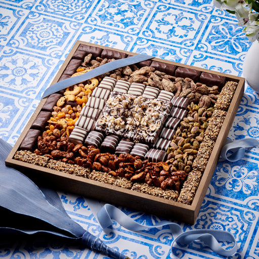 Beautifully arranged chocolate and nut gift tray featuring a variety of treats, displayed on a blue patterned tablecloth with a matching ribbon.
