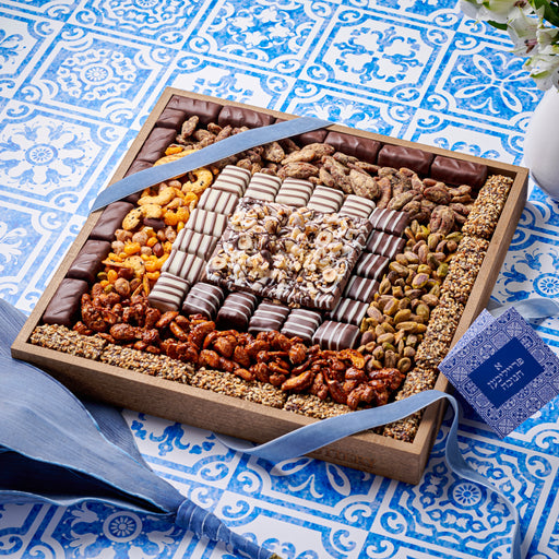 Square wooden tray filled with an assortment of gourmet chocolates, nuts, and dried fruits, elegantly tied with a blue ribbon for gifting.
