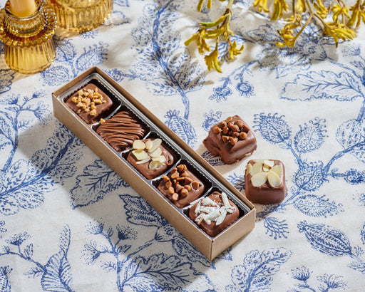 A long box of Nuttery Halva Bites against a sleek flower-themed  backdrop, highlighting their rich texture and toppings.