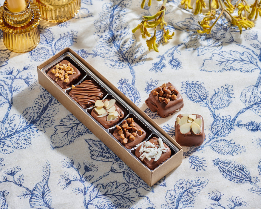 A long box of Nuttery Halva Bites against a sleek flower-themed  backdrop, highlighting their rich texture and toppings.