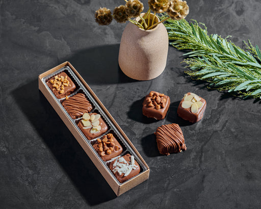 A luxurious box of Nuttery Halva Bites against a sleek black backdrop, highlighting their rich texture and toppings.