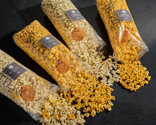 Four bags of gourmet popcorn in assorted flavors, including caramel, cheddar, and sweet mix varieties, spilling out onto a black tabletop for a vibrant display.