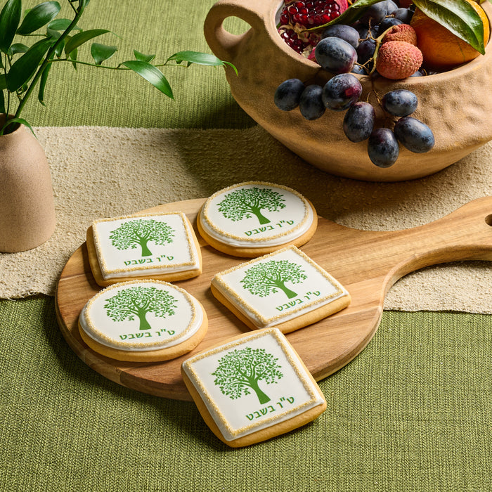 A collection of square and round sugar cookies with Tu B’Shvat tree-themed decorations in green and gold icing, arranged on a wooden serving board.