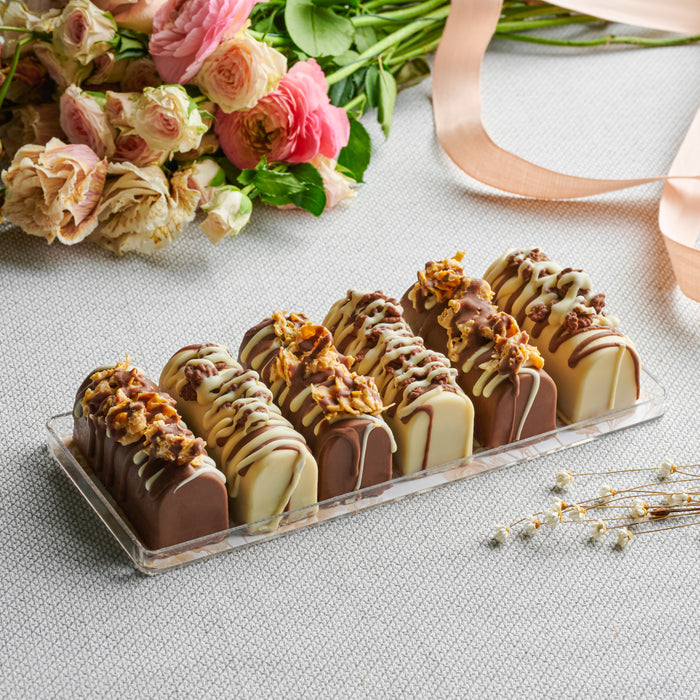 Elegantly packaged mini cheese logs in a clear gift box, adorned with a delicate ribbon and floral accent, making it a stunning Shavuot gift or indulgent treat.