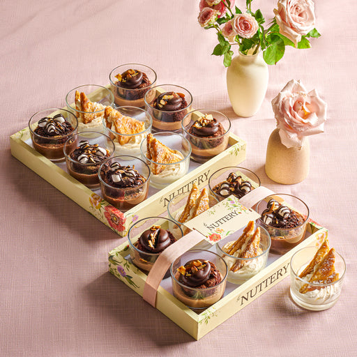 An assortment of rich chocolate and vanilla mousse cups displayed in a gift-ready Nuttery presentation tray, with floral decor in the background.