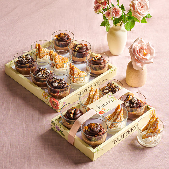 An assortment of rich chocolate and vanilla mousse cups displayed in a gift-ready Nuttery presentation tray, with floral decor in the background.