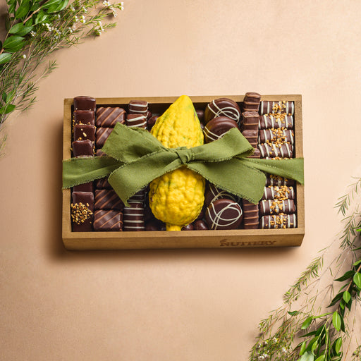 A rustic display of chocolate-drizzled s'mores popcorn spilling from a burlap sack, accompanied by graham crackers, marshmallows, and chocolate pieces on a wooden surface