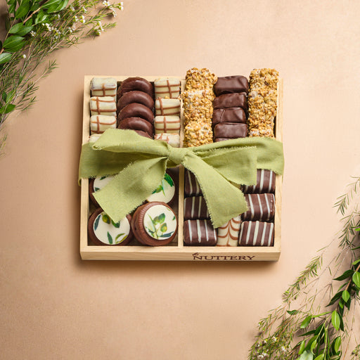 Small wooden platter featuring four sections of assorted chocolates and treats, wrapped with a green ribbon and surrounded by greenery for Sukkot celebrations