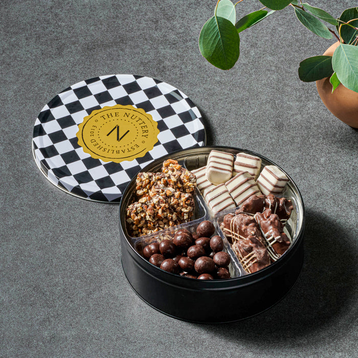 The Nuttery NY gourmet chocolate and nut tin, featuring a premium assortment of chocolate-covered treats, nut clusters, and artisanal confections, elegantly packed in a stylish checkered tin.