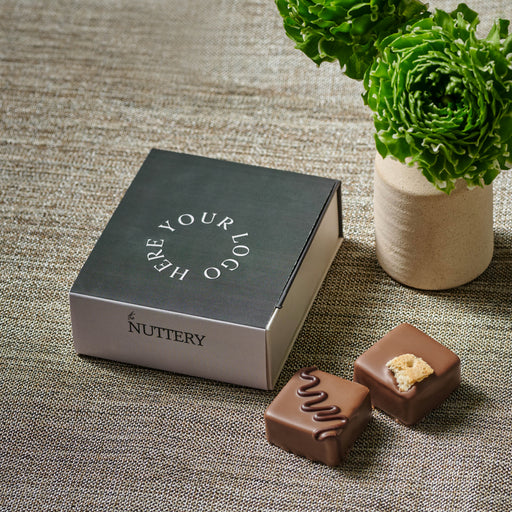 Open mini truffle box showcasing four handcrafted dairy chocolates with intricate designs, paired with fresh greenery for a sophisticated presentation.