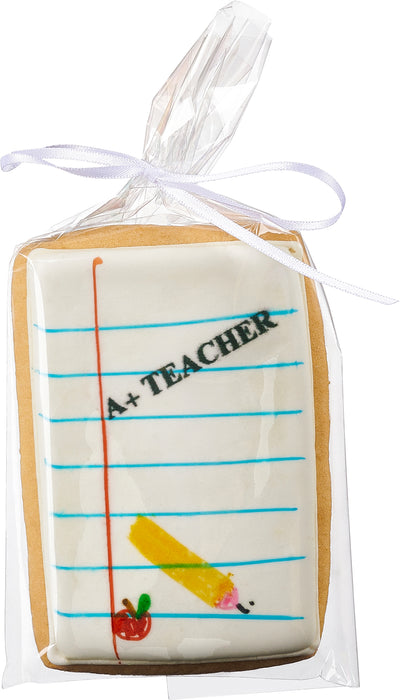 A decorated sugar cookie shaped like a notepad, featuring an "A+ Teacher" message with a pencil and apple design, individually wrapped for a thoughtful teacher appreciation gift.