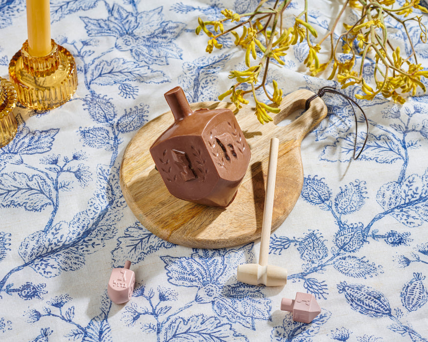 Hanukkah chocolate smash dreidel from The Nuttery NY, displayed on a vibrant blue and pink background with scattered candy, chocolate pieces, and a dreidel, highlighting its festive and interactive appeal.