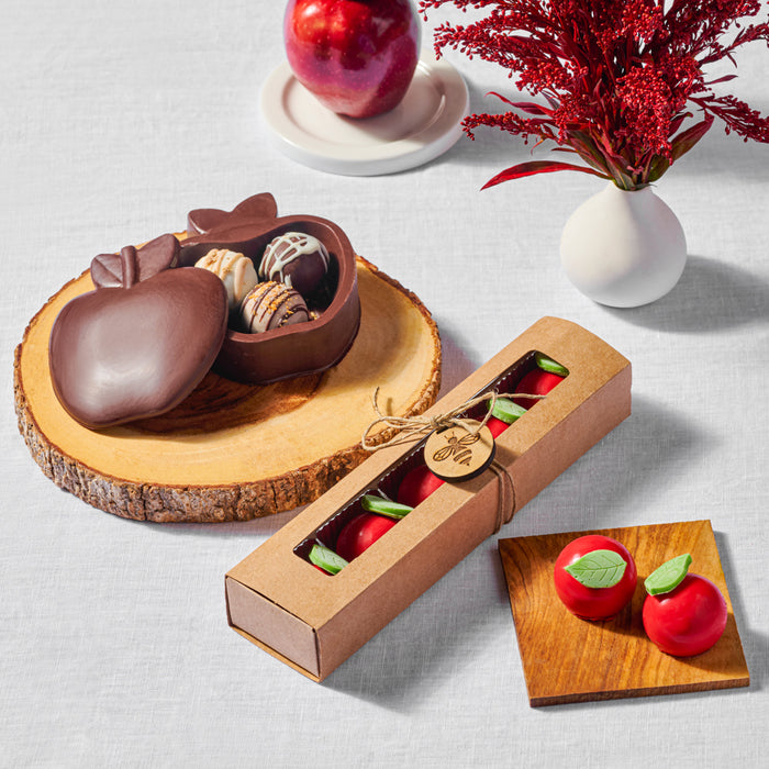 Chocolate apple-shaped box filled with gourmet truffles, displayed on a wooden slice with apples in the background and flowers