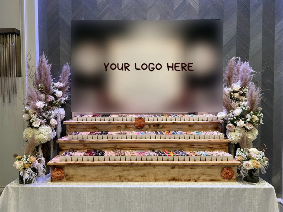 A grand floral-inspired display of gourmet chocolates, nuts, and candy arranged in a tiered setup. Perfect for events, this luxurious spread brings elegance and indulgence together.