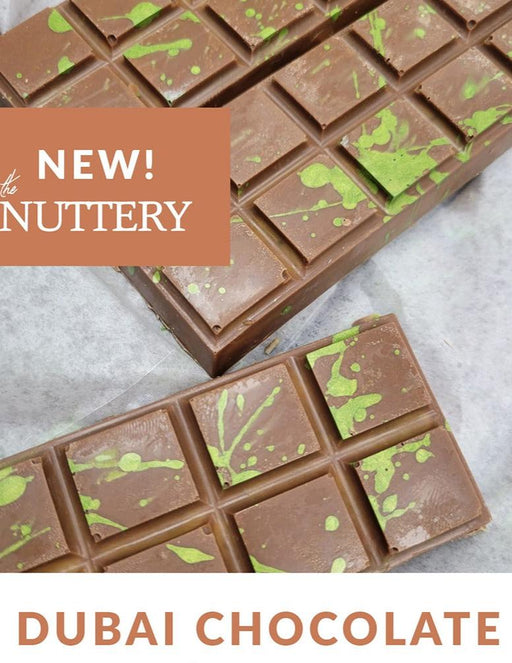Elegant Dubai chocolate bars presented on a sleek slate platter, surrounded by warm lighting and floral accents. A sophisticated treat for special occasions or gourmet gifting.