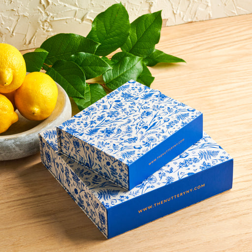 A small blue and white floral gift box from The Nuttery, elegantly designed for gourmet treats and premium gifts.