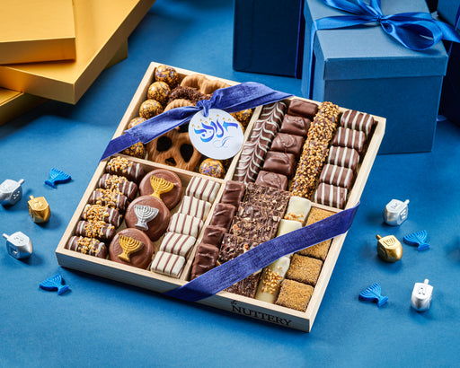 The Nuttery NY Hanukkah chocolate and nut gift trays, elegantly arranged with gourmet chocolates, menorah-themed treats, and crunchy nut selections, wrapped in festive blue ribbons for the holiday season.