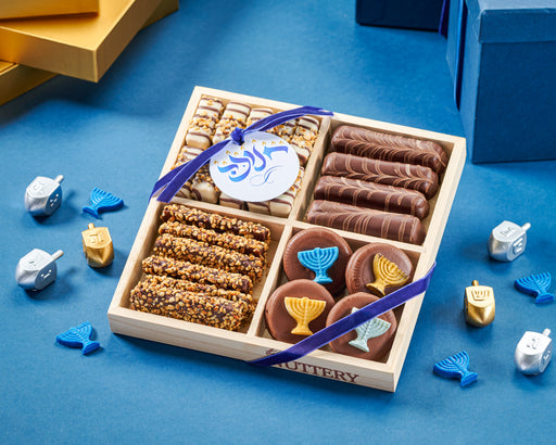 The Nuttery NY Chanukah chocolate delight tray, featuring a festive assortment of menorah-decorated chocolate cookies, nut clusters, and gourmet chocolate-covered treats, elegantly packaged with a blue holiday ribbon.