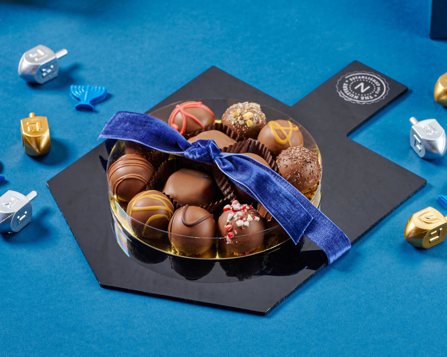The Nuttery NY Dreidel Truffle Tray, a Hanukkah-themed gift featuring an assortment of gourmet chocolate truffles, elegantly arranged on a dreidel-shaped tray and tied with a festive blue ribbon.