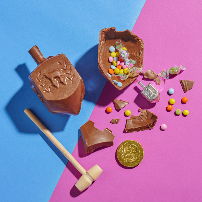 The Nuttery NY Hanukkah mini chocolate smash dreidel, crafted from rich milk chocolate and featuring traditional Hebrew engravings, presented with a wooden mallet for a fun and festive treat.