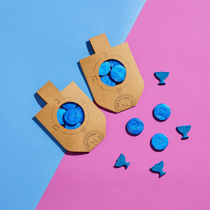 Chanukah dreidel-shaped card filled with blue chocolate coins, arranged on a vibrant pink and blue background alongside menorah-shaped decorations.