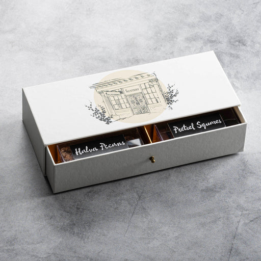 Unopened gift box featuring an illustration of The Nuttery storefront, filled with an assortment of gourmet chocolates, nuts, and specialty confections.