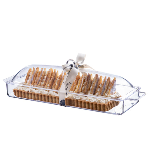 Rectangular tart topped with white chocolate curls and creamy frosting, presented in a clear acrylic serving tray and tied with a branded cream ribbon, perfect for celebrations.