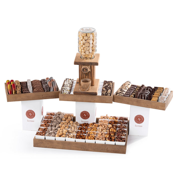 Elegant wooden nut dispenser tower surrounded by a gourmet selection of chocolate-covered treats, nut clusters, and confectionery, perfect for gifting or events