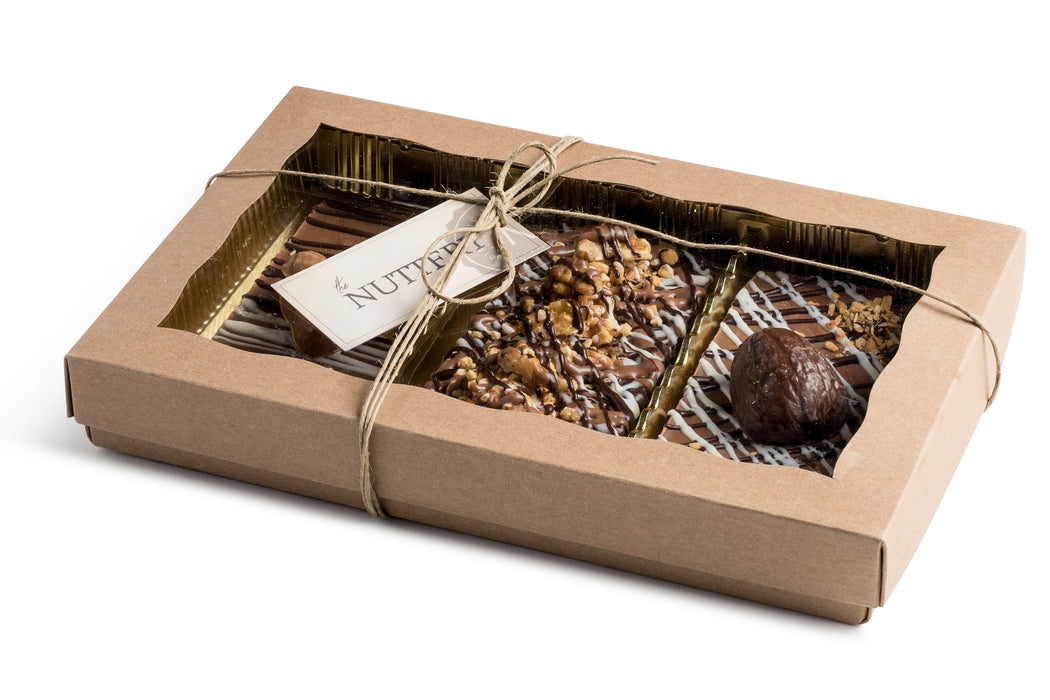 An open view of The Nuttery’s gourmet tart box, revealing three chocolate tarts with various toppings, including nuts, cookie crumbles, and white chocolate drizzle.