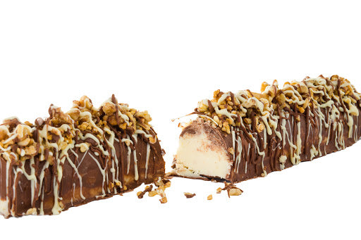 A beautifully packaged cheese log dessert, enclosed in a clear gift box with a sturdy handle, adorned with caramel drizzle, pecans, and white chocolate accents for a luxurious presentation.