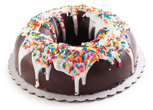 The Nuttery NY chocolate candy smash cake, a festive ring-shaped cake coated in rich chocolate, topped with white icing and colorful sprinkles, designed to be cracked open for a surprise-filled treat.