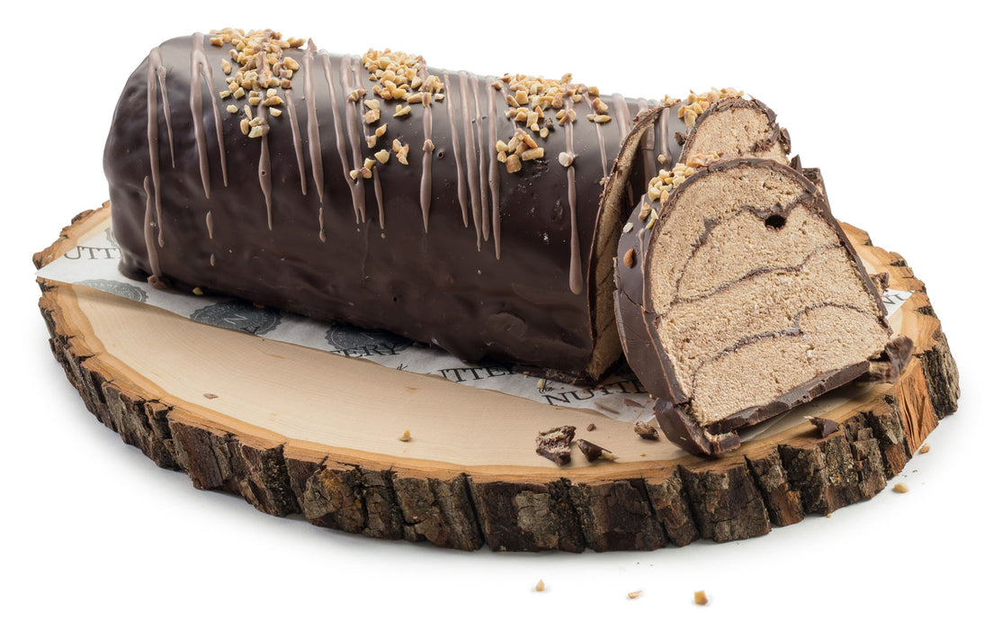 A rich and decadent halvah zebra log covered in smooth dark chocolate, drizzled with chocolate ribbons, and sprinkled with crushed nuts. Sliced to reveal a marbled sesame-based filling, this gourmet dessert sits on a rustic wooden serving board for an artisanal presentation.
