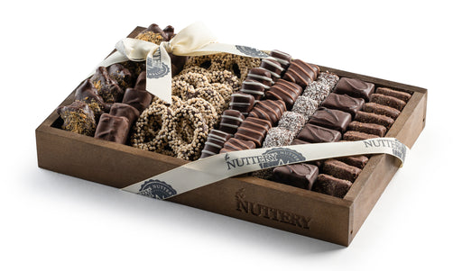A premium wooden gift tray packed with an assortment of chocolate-covered treats, including pretzels, nougat, and nut clusters, elegantly wrapped with a ribbon.