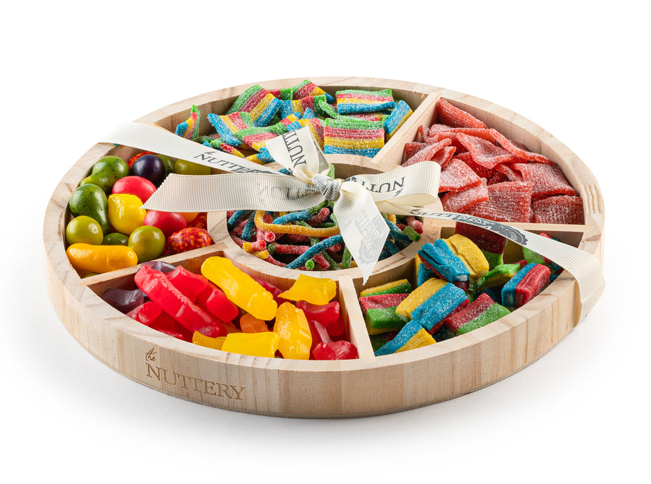 Large wooden gift tray with six sections filled with assorted colorful candies, including sour belts, gummy bears, and fruit-shaped treats, wrapped with a decorative ribbon.