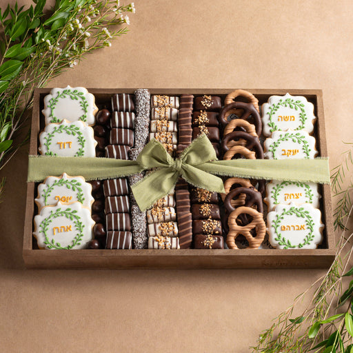 A premium wooden gift tray featuring handcrafted Ushpizin-themed cookies, gourmet chocolates, and chocolate-covered pretzels, elegantly tied with a green ribbon.