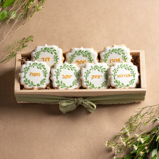 A handcrafted cookie crate featuring six Ushpizin-themed sugar cookies with Hebrew names, decorated with green leaf accents and gold lettering.
