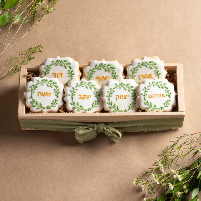A handcrafted cookie crate featuring six Ushpizin-themed sugar cookies with Hebrew names, decorated with green leaf accents and gold lettering.