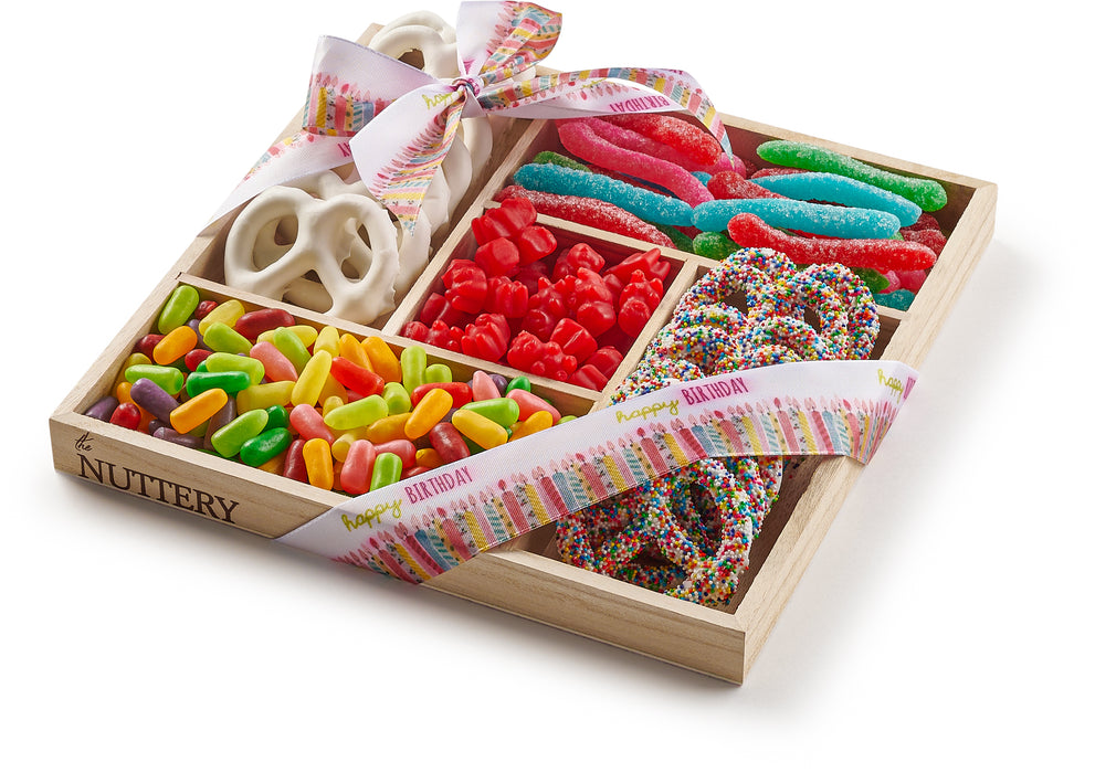 Birthday-themed wooden gift tray featuring five sections of candies and chocolates, including chocolate-covered pretzels, cherry gummies, sour worms, and jelly sticks, tied with a festive ribbon.