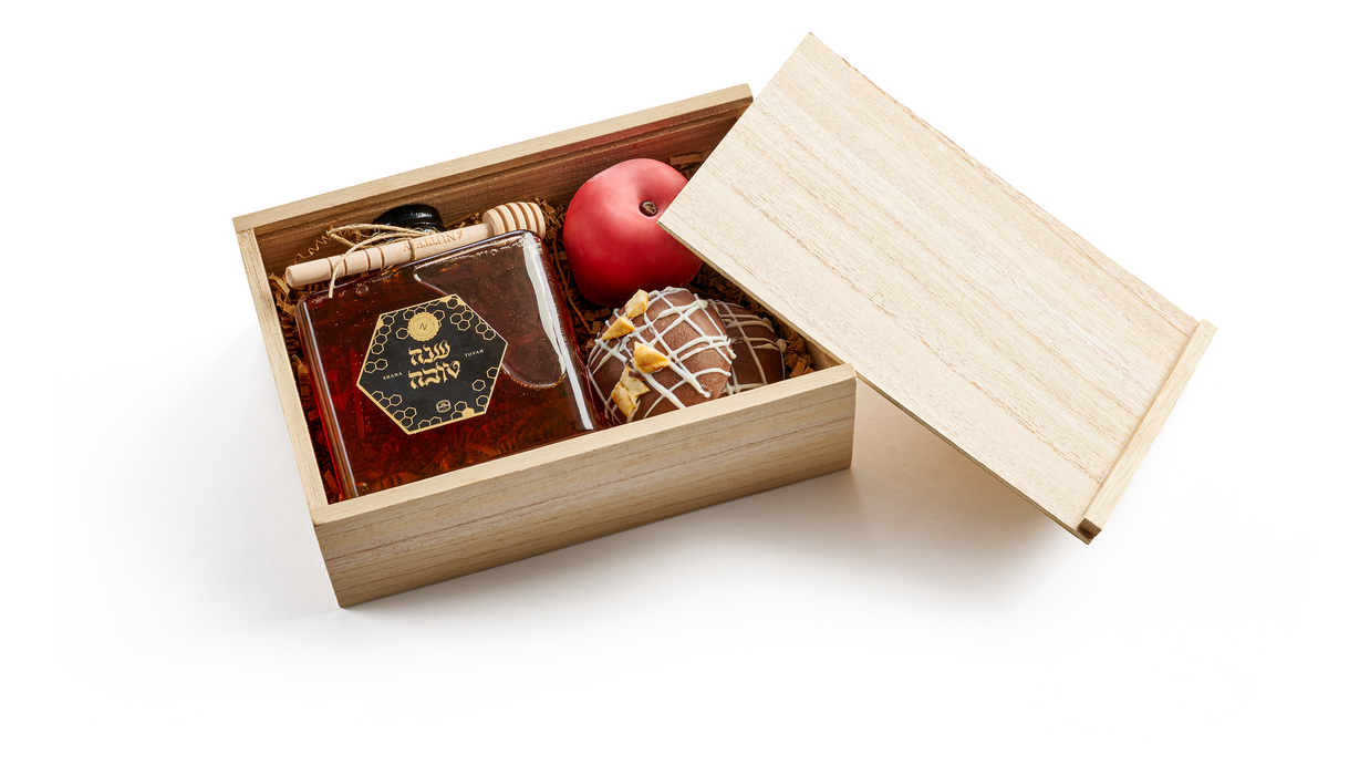 A wooden gift crate containing a jar of honey, a decorative red chocolate apple, and gourmet chocolate truffles, perfect for Rosh Hashanah gifting