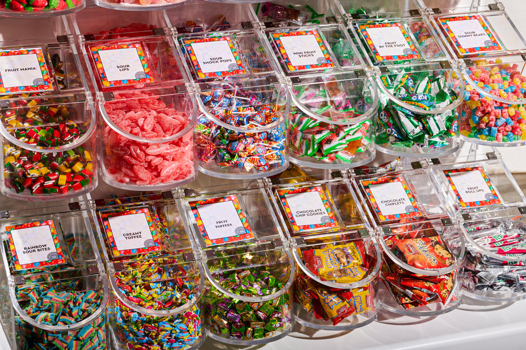 Close-up of candy bins showcasing various sweets like sour lips, rainbow sour bites, and chocolate chip cookies.