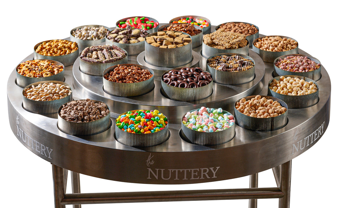 A luxurious round table display featuring an assortment of gourmet nuts, chocolates, and candies arranged in metal tins, perfect for events or celebrations